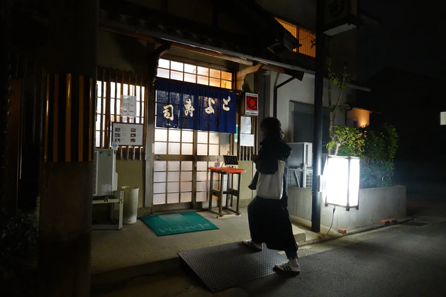 The warm, intimate interior of a traditional sushi restaurant in Kyoto at night.